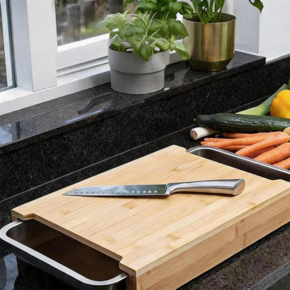 Planche à découper bambou avec tiroirs présentation de la planche a demi ouverte ou l'on distingue le tiroir au dessus de la planche est posé un couteau, a coête des légumes 